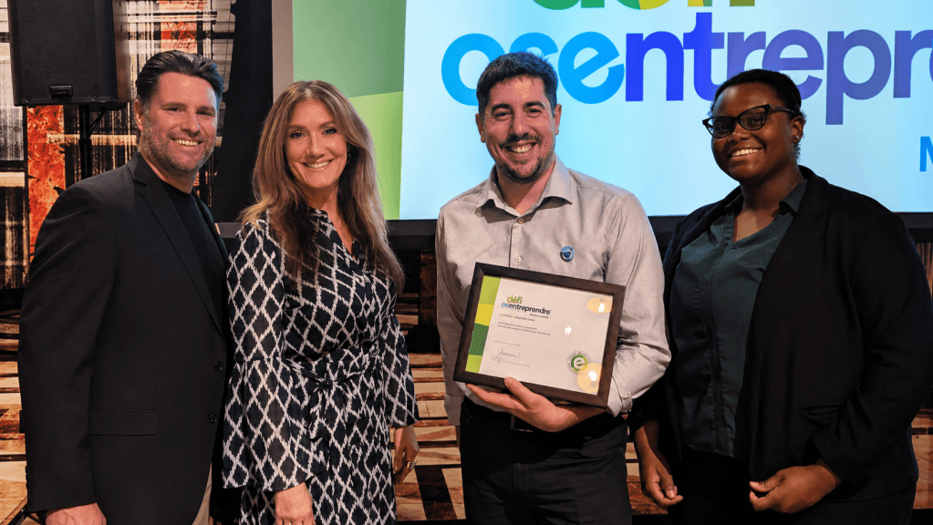Four professionals pose on stage; the man in the center holds a framed certificate while the others smile nearby.