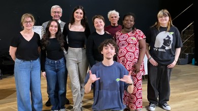 Group of ten people posing together on a stage, smiling at the camera, casual attire