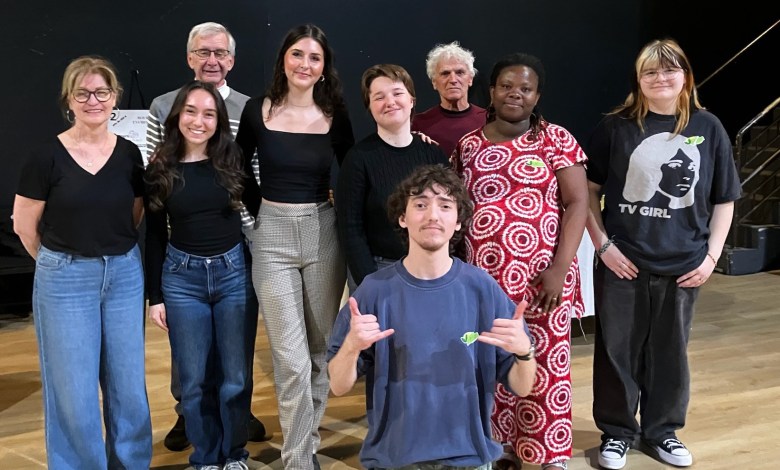 Group of ten people posing together on a stage, smiling at the camera, casual attire