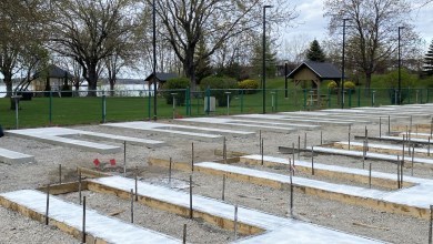 Construction site with concrete slabs and wooden forms for future foundations near a lakeside park.