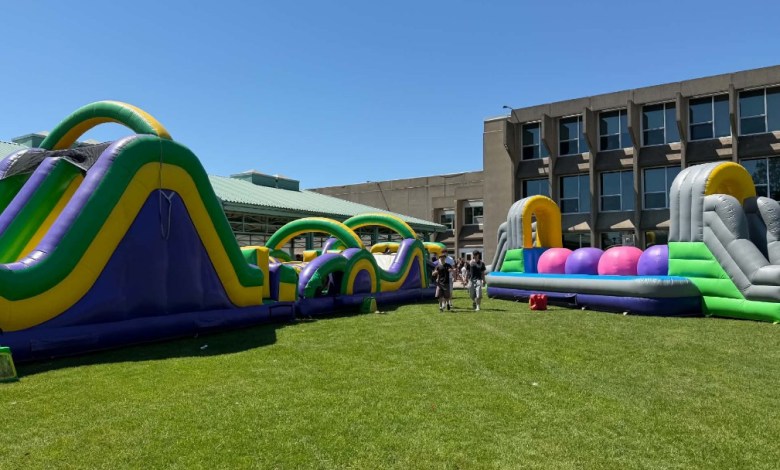 Colorful inflatable obstacle course set up on a grassy field beside a modern building; several people stand nearby on a sunny day.