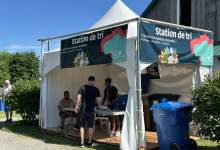 Outdoor recycling station tent with a blue banner reading Station de tri and people standing under it.