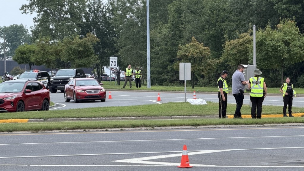Roadside incident scene with police in high-visibility vests directing traffic and several cones on a multi-lane road at daytime.