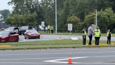 Roadside incident scene with police in high-visibility vests directing traffic and several cones on a multi-lane road at daytime.